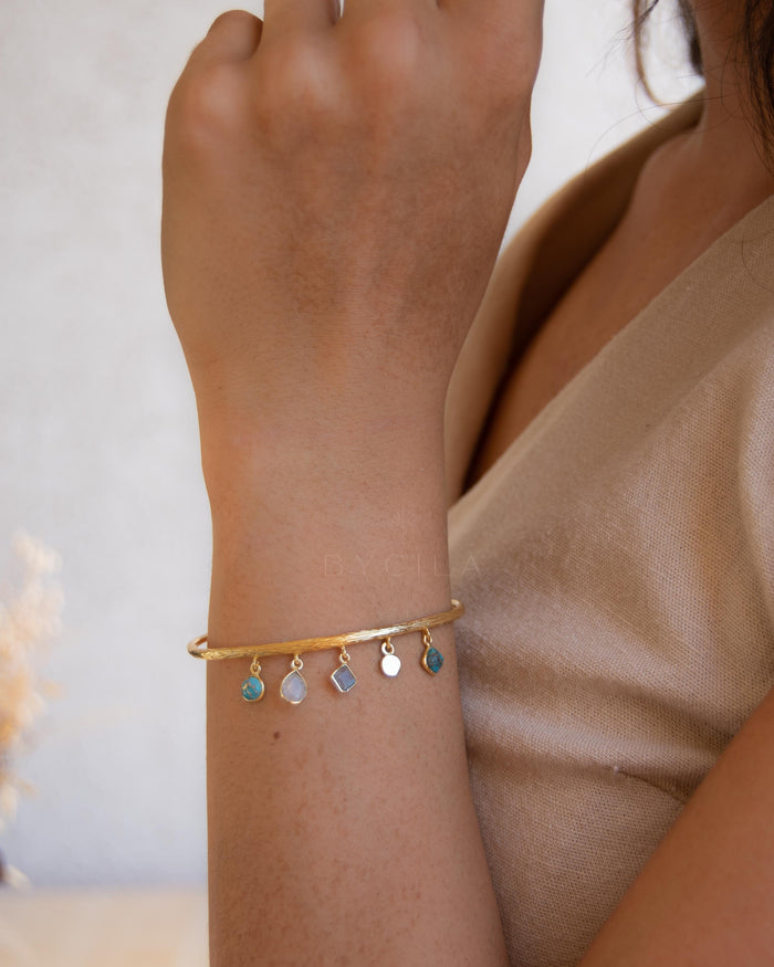 Gold bracelet with colorful charms on a wrist against a neutral background