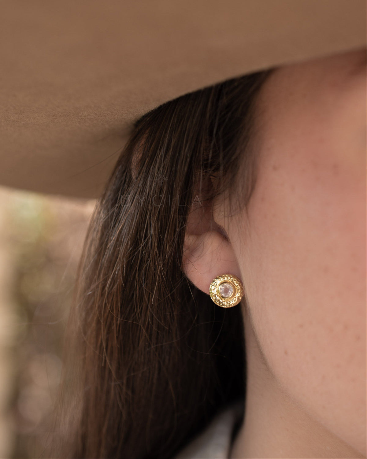 Close-up of a person wearing a gold earring with a blurred background