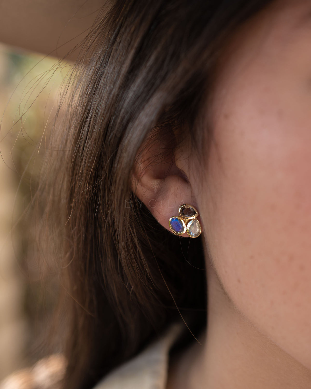 Close-up of an ear wearing a gold earring with a blue gemstone.