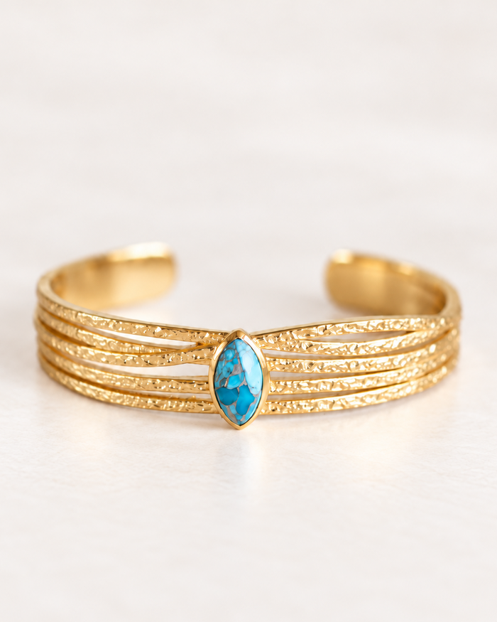 A gold multi-band cuff bracelet featuring a marquise-cut blue stone in the center, set against a clean white background.