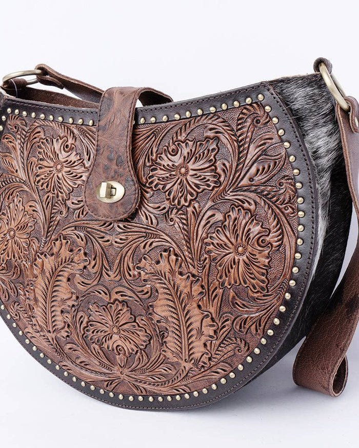 Brown leather handbag with intricate floral patterns on a white background